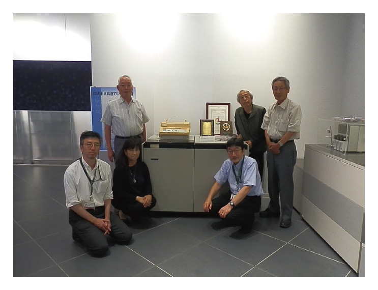 Fig. 5 Hitachi's Model 835 High-Speed Amino Acid Analyzer with its developers and the authors of this article. Back row, from left: Hiroshi Satake (mechanics), Yoshio Fujii (analysis), Akira Numata (testing).<br>
Front row, from left: Norimasa Minamoto, Yoko Inoue, Masahito Matt Ito.