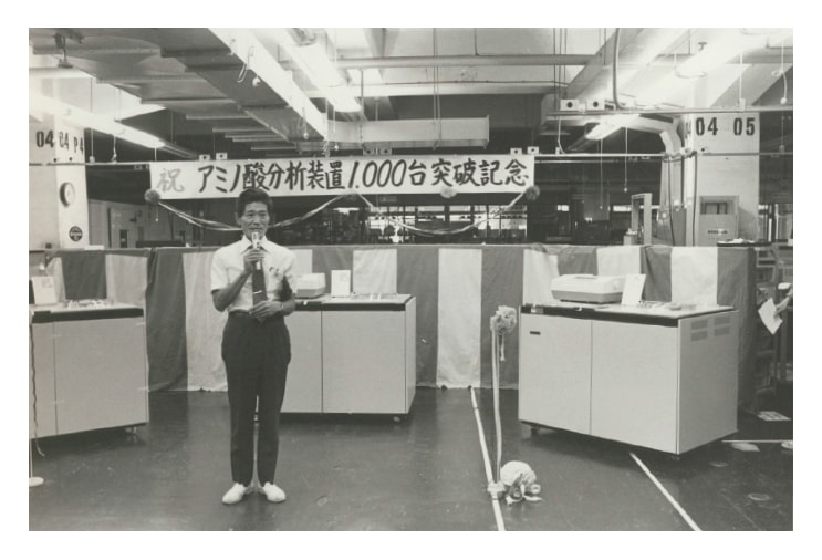 Fig. 6 Dr. Shigetake Ganno congratulating workers at a Hitachi production site during a ceremony commemorating the 1,000th shipped Model 835 unit.