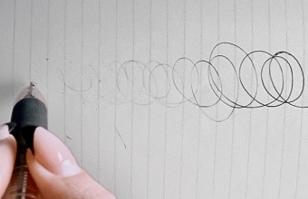 重力（じゅうりょく）が働（はたら）かないように天井（てんじょう）を向（む）いてボールペンで書（か）く様子（ようす）