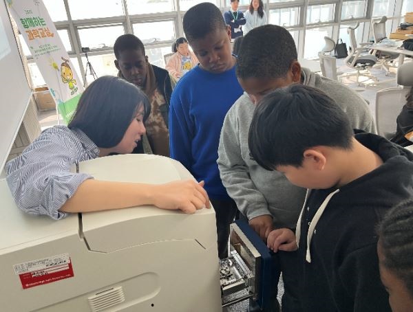 Observing the inside of a tabletop electron microscope while receiving an explanation from a Hitachi High-Tech Korea employee